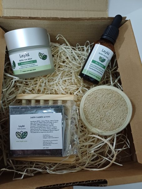 Caja con productos de cuidado de la piel: crema, aceite y jabón sobre cama de papel.